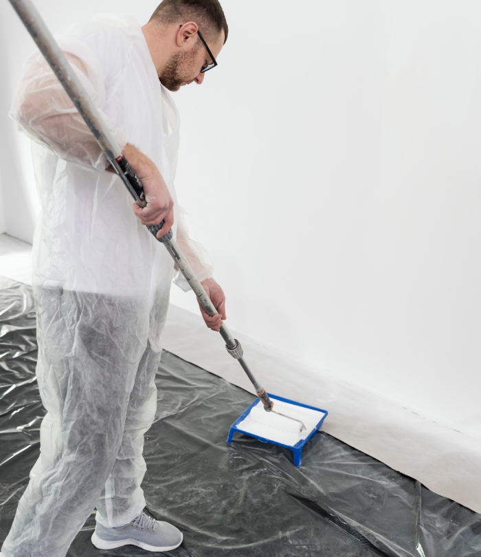 Professionnel en combinaison appliquant un produit de décapage sur un mur intérieur avant rénovation.