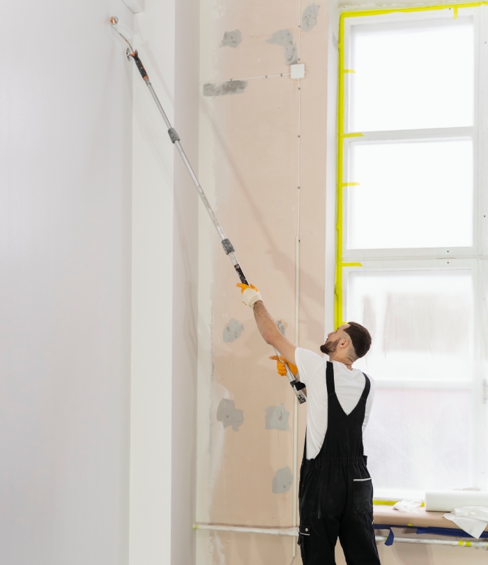 Peintre professionnel appliquant de la peinture sur un mur intérieur en cours de rénovation.