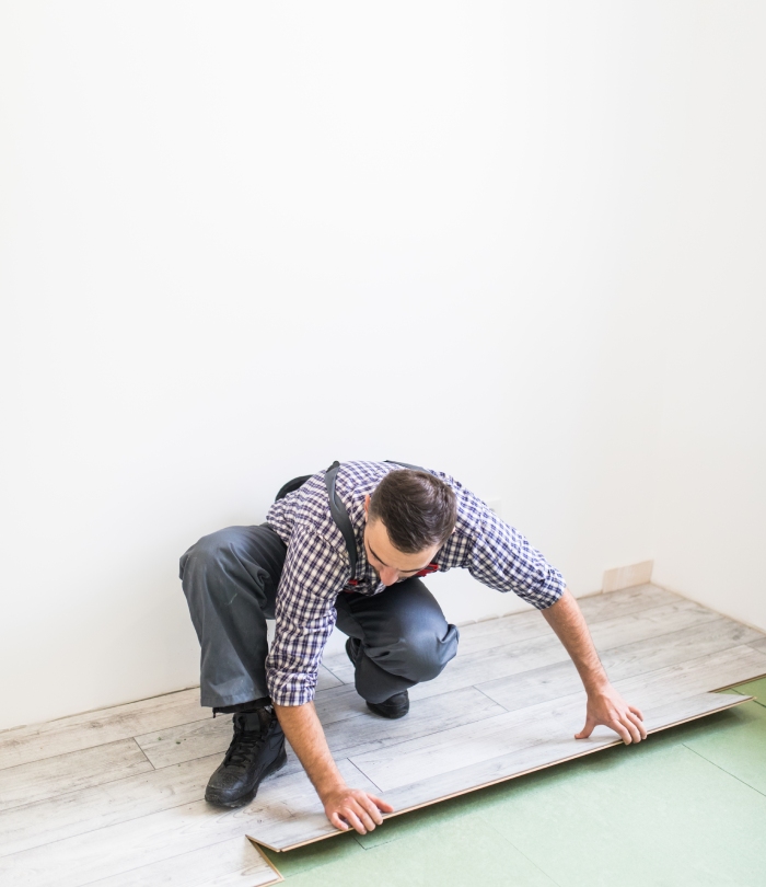 Artisan posant une lame de parquet flottant dans une pièce en rénovation.