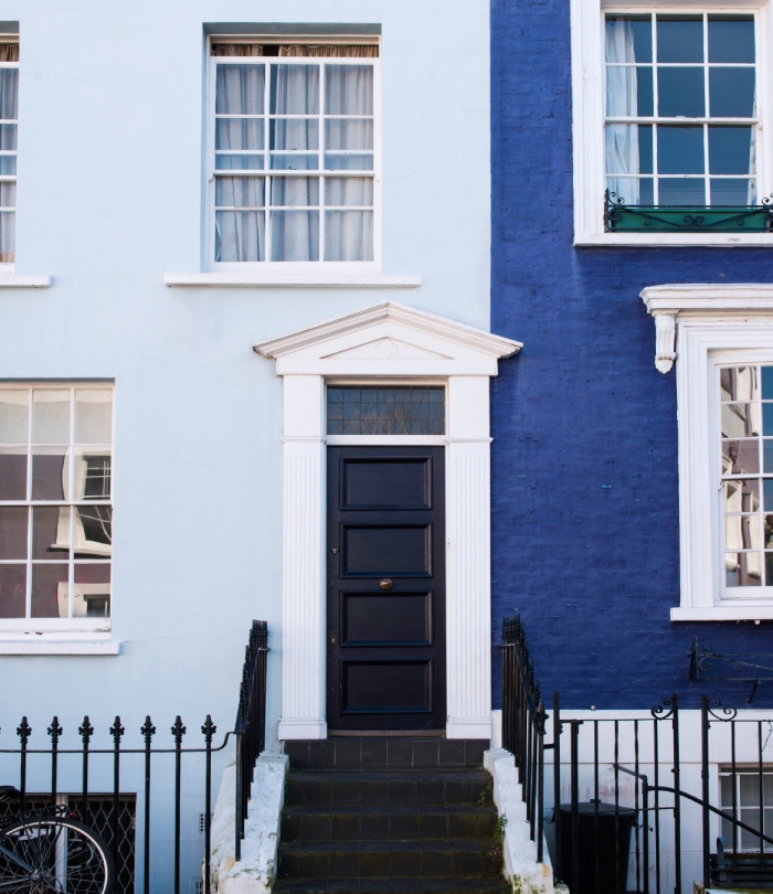Façade de maison rénovée avec peinture extérieure blanche et bleue autour d’une porte d’entrée.